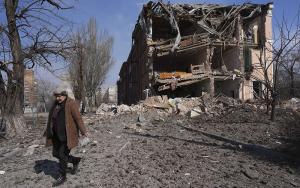 A woman walks past building damaged by shelling in Mariupol, Ukraine, Sunday, March 13, 2022. The surrounded southern city of Mariupol, where the war has produced some of the greatest human suffering, remained cut off despite earlier talks on creating aid or evacuation convoys.