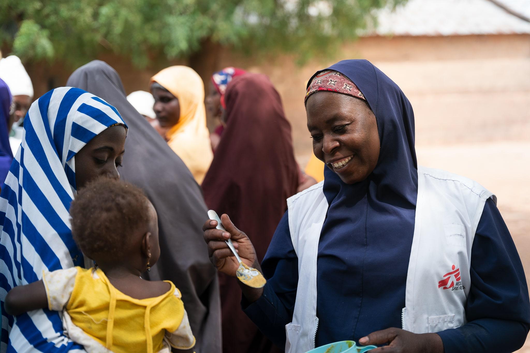 Acute Malnutrition in Nigeria: Maryam Muhammad, MSF health promotion supervisor in Kebbi, gives a spoon of Tom Brown to a child during a recipe demonstration in Maishaka village, Kebbi State, North West Nigeria. Around a hundred women participated in this demonstration.