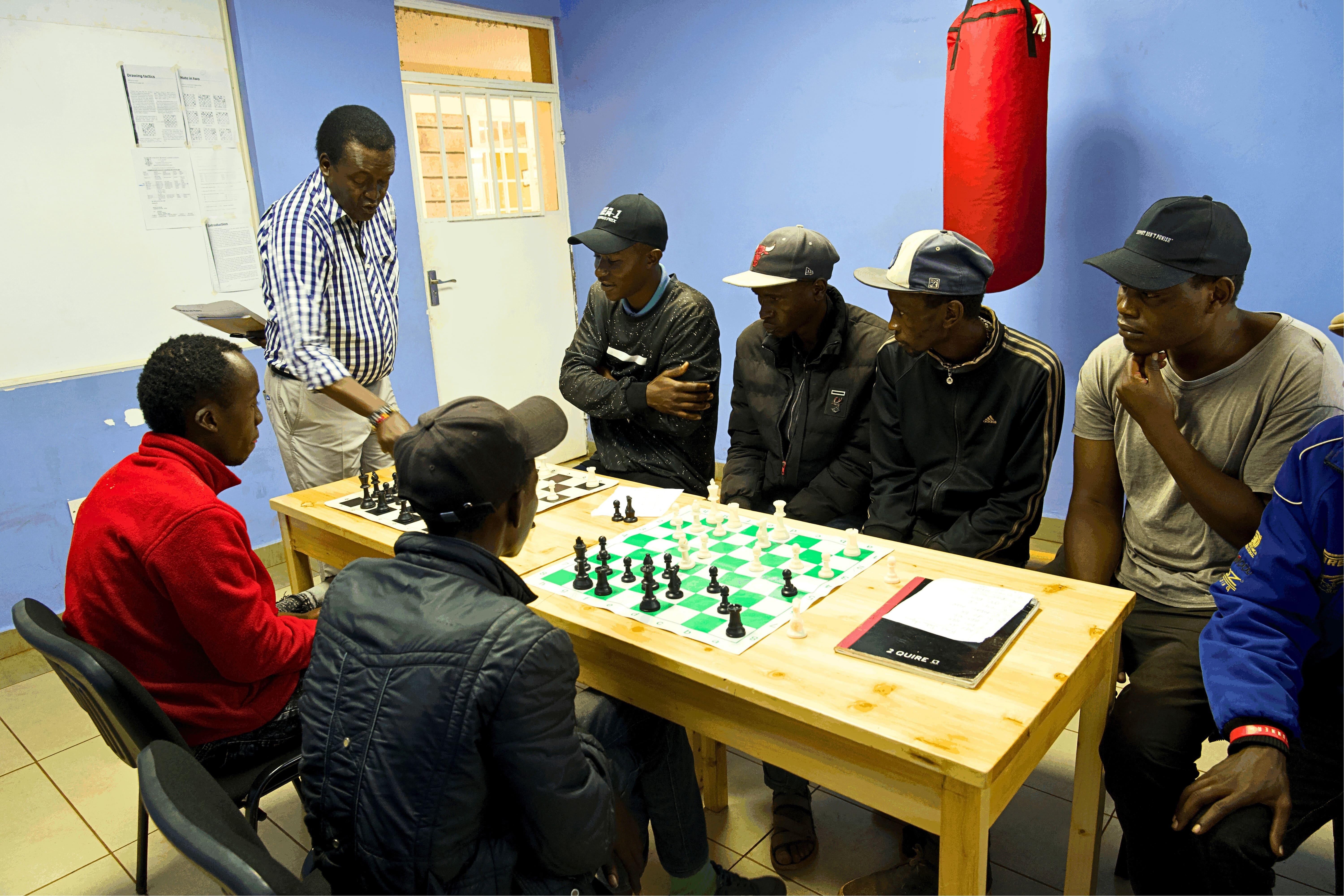 Treatment of People Who Use Drugs in Kenya: Coach Patrick standing, guides his learners as he trains them on Chess at the Karuri medically assisted therapy clinic empowerment center.